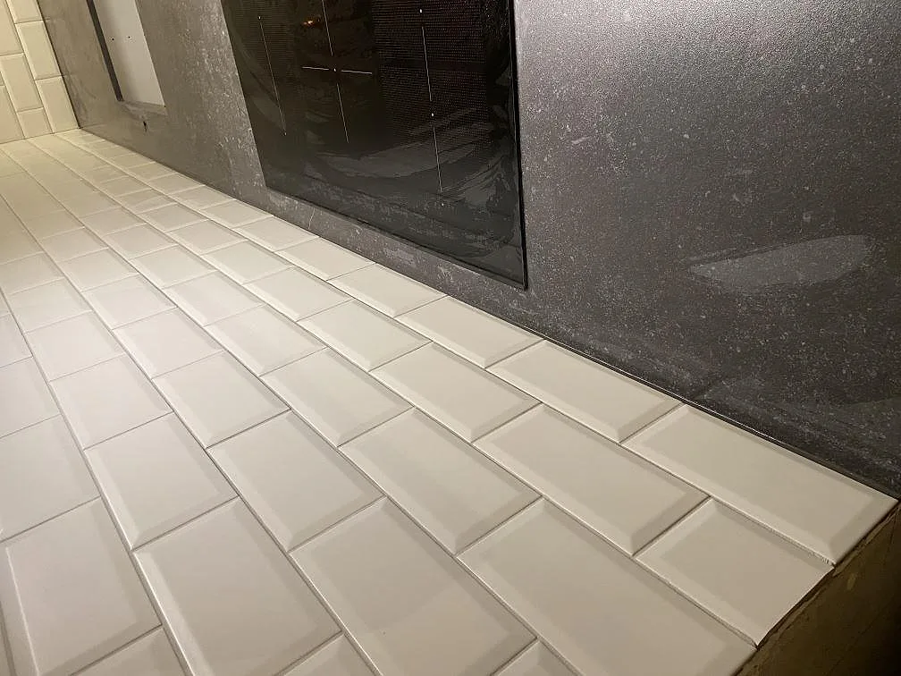 Detalj av mörk Dekton Fossil köksbänkskiva som möter vitt fasat kakel i ett kök i Höllviken.
