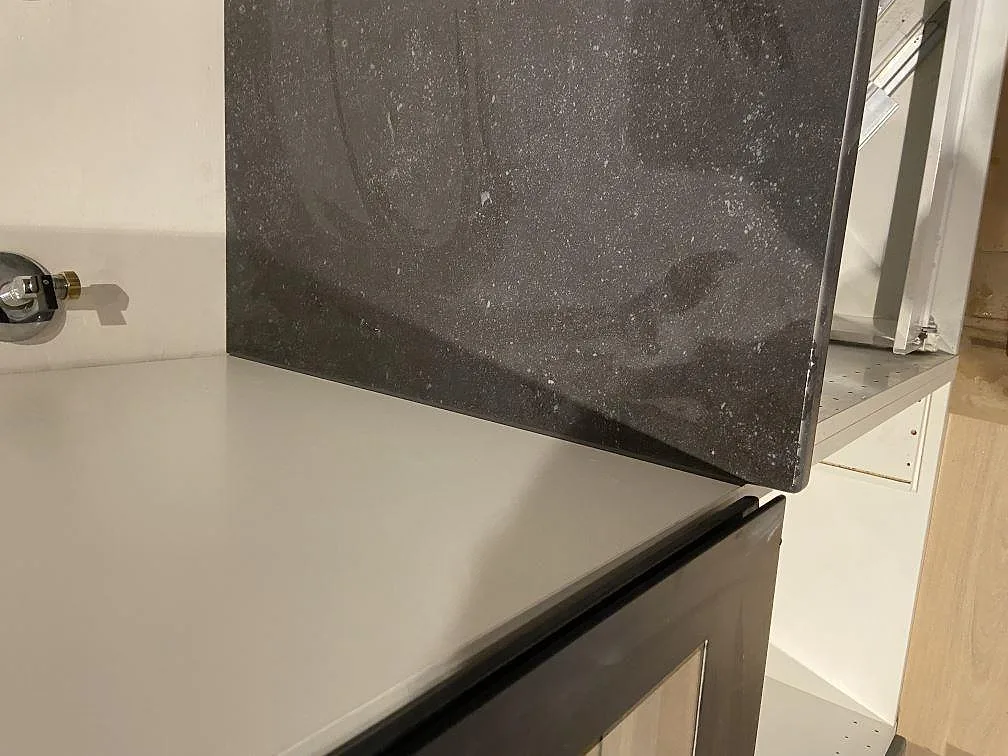 Översiktsbild av köksbänkskiva i Dekton Fossil längs väggen med stänkkant och vitt kakel under montering i Höllviken.