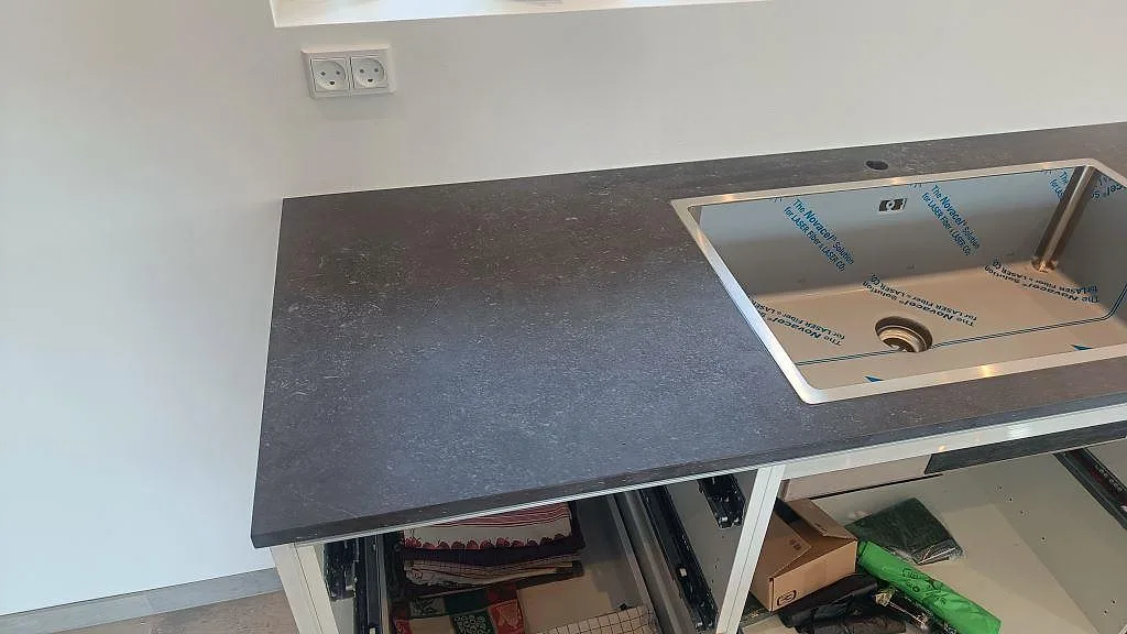 Matt bänkskiva i Dekton Fossil keramik med rostfri diskho och öppna köksstommar under montering i Jyllinge.