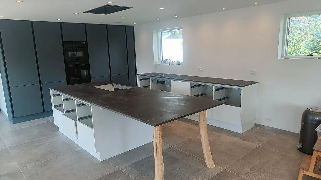 Matt köksbänkskiva i Dekton Fossil keramik med stor köksö, bänk längs väggen och hällurtag i ett kök i Jyllinge.