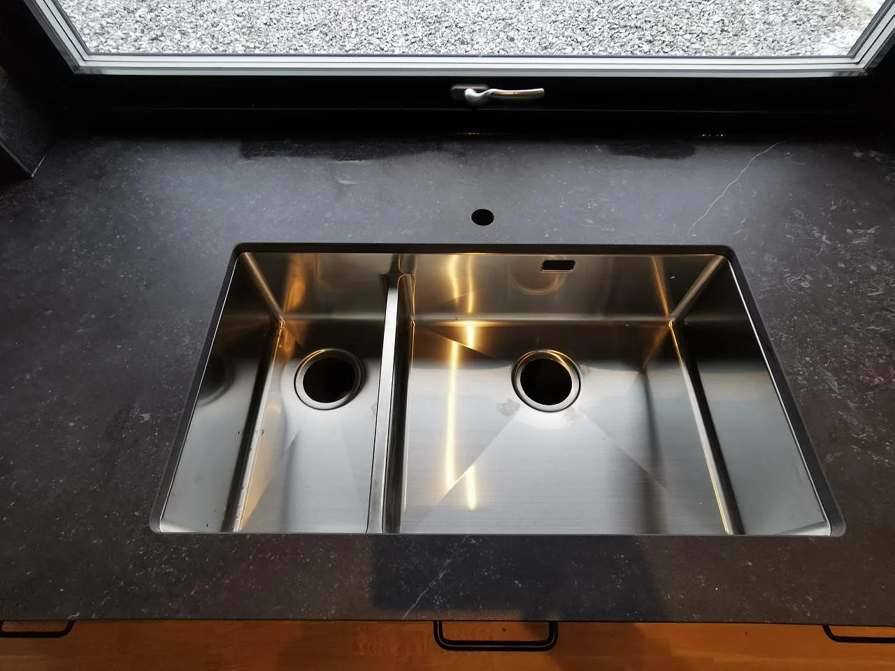 Närbild på underlimmad dubbel rostfri Strand-diskho infälld i en matt Dekton Fossil köksbänkskiva i Landvetter.