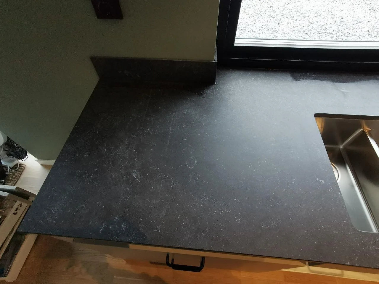 Hörn av köksbänkskiva i mörk Dekton Fossil med underlimmad rostfri diskho och stänkskydd i samma sten i ett kök i Landvetter.