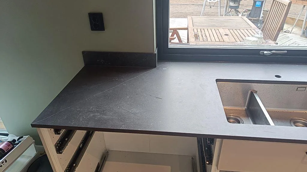 Detalj av matt Dekton Fossil som köksbänkskiva med diskho och mörk stänkkant i Landvetter.