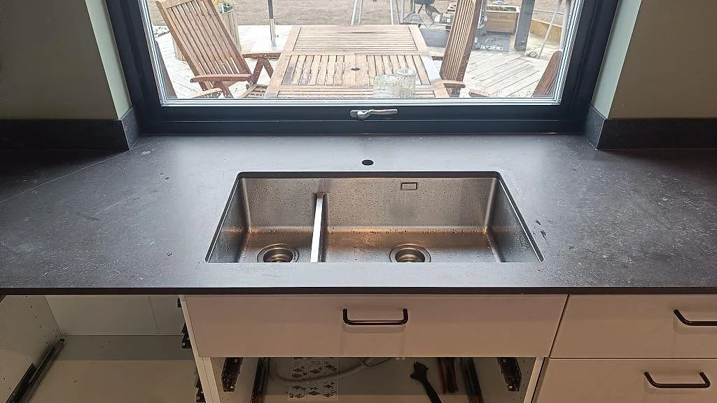 Närbild på matt köksbänkskiva i Dekton Fossil med dubbel diskho vid fönster i Landvetter.
