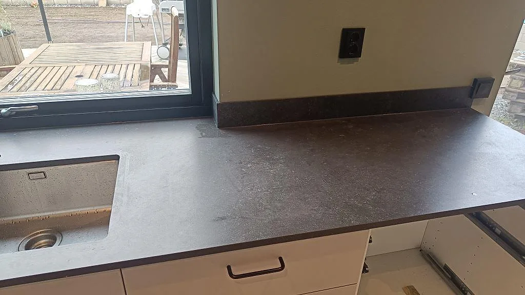 Högersida av köksbänkskiva i matt Dekton Fossil med låg stänkkant och synlig diskho i Landvetter.