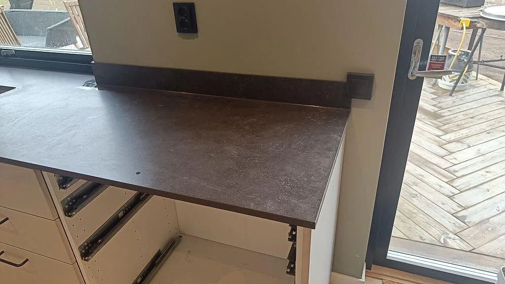 Detalj av matt köksbänkskiva i Dekton Fossil med låg stänkkant mot vägg och altandörr i Landvetter.