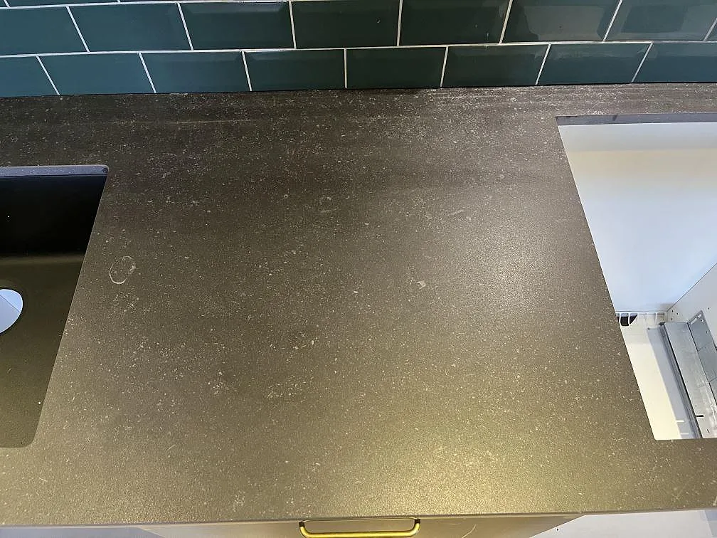 Närbild på matt Dekton Fossil köksbänkskiva i keramik med dess rostbruna ton mot grön kakel i ett kök i Timmele.