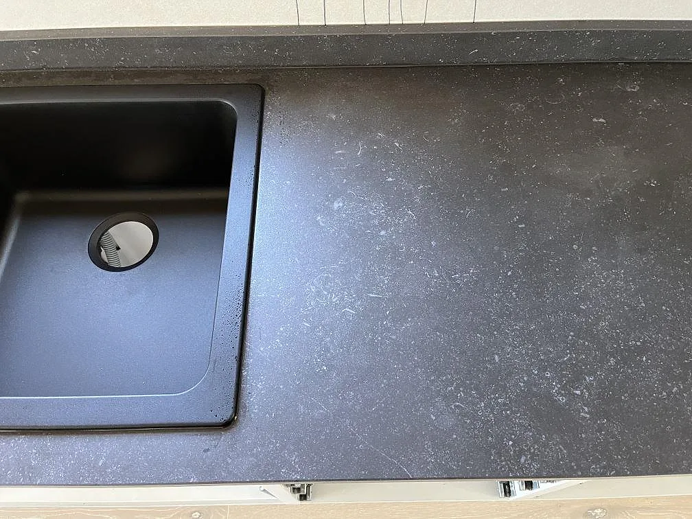 Köksbänkskiva i Dekton Fossil med uppvikt stänkkant mot väggen, matt mörk yta med diskret ådring, i ett kök i Uddevalla.