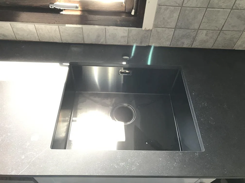 Hörnparti av köksbänkskiva i mörk Dekton Fossil med matt yta mot ljust kakel i ett kök i Vellinge.