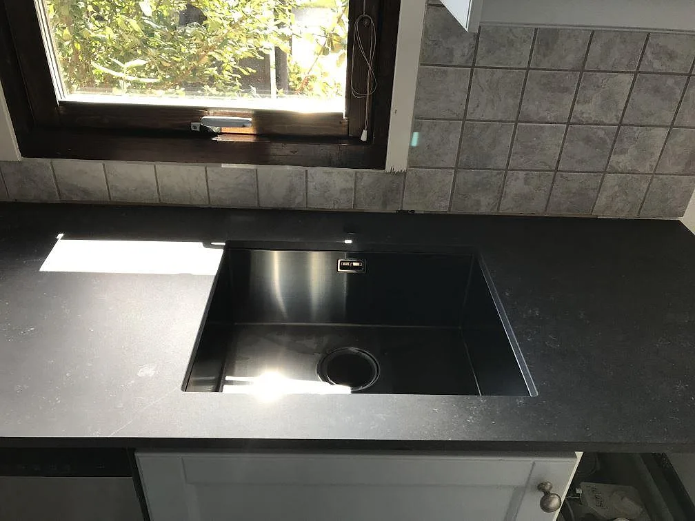 Köksbänkskiva i matt antracitgrå Dekton Fossil mot ljusgrått kakel i ett kök i Vellinge.