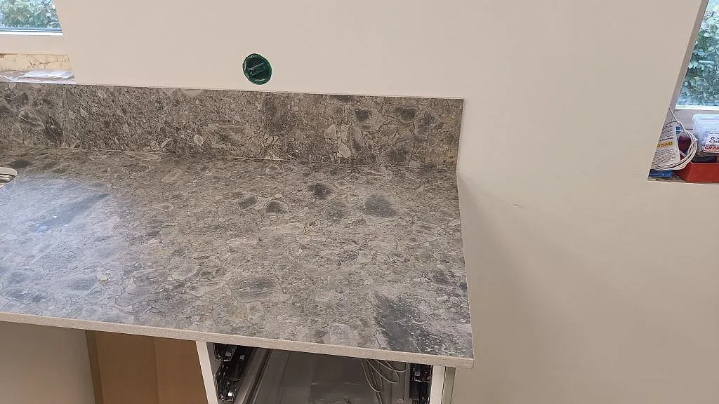 Bänkskiva och stänkkant i matt Dekton GK07 Ceppo med grå stenlook vid fönstervägg i Össjö.