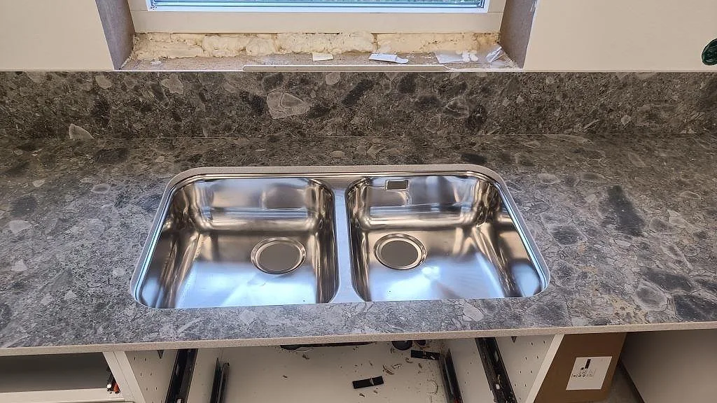 Dubbel rostfri diskho underlimmad i matt Dekton GK07 Ceppo med låg stänkkant i ett kök i Össjö.