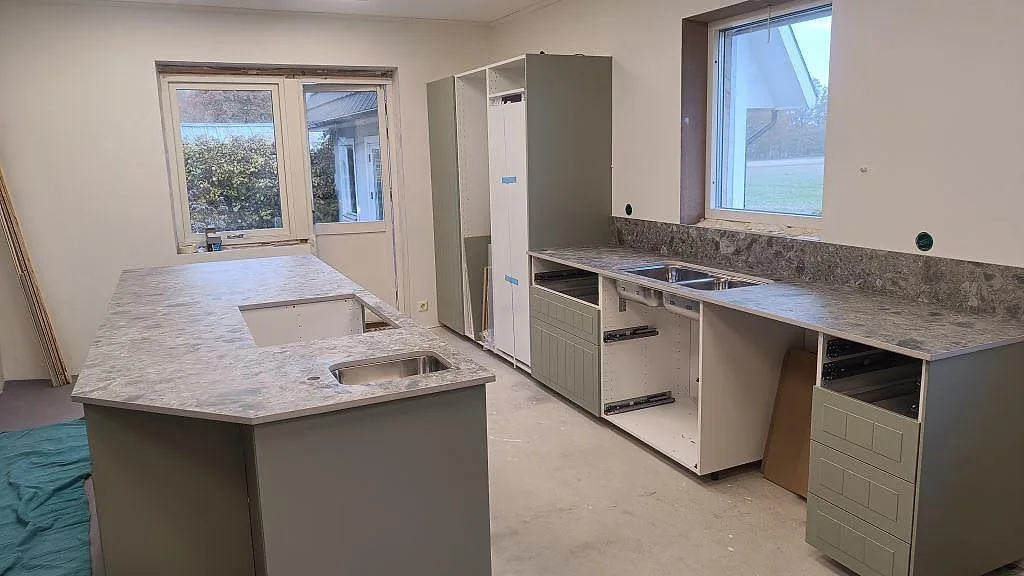 Köksbänkskiva i matt Dekton GK07 Ceppo med köksö, bänkrad och rostfria diskhoar under montering i Össjö.