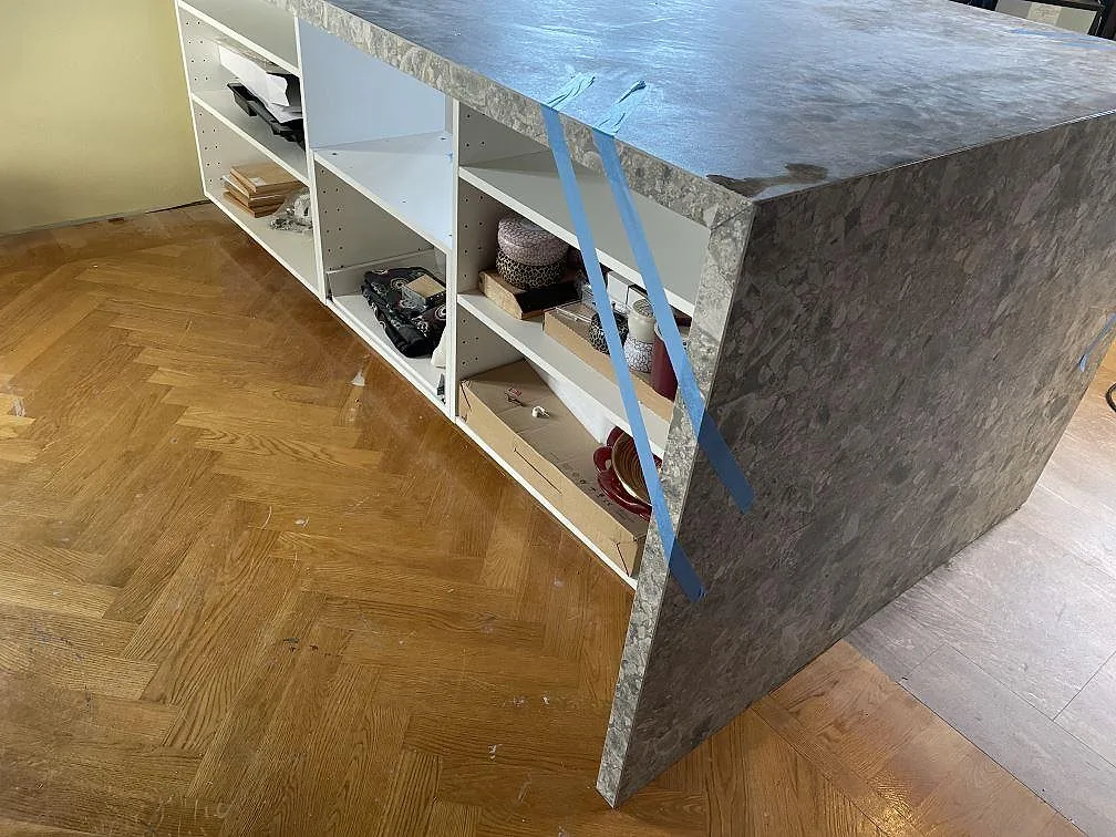 Sidoklädd köksö i matt Dekton GK07 Ceppo med grå stenlook och fiskbensparkett i ett kök i Västra Frölunda.