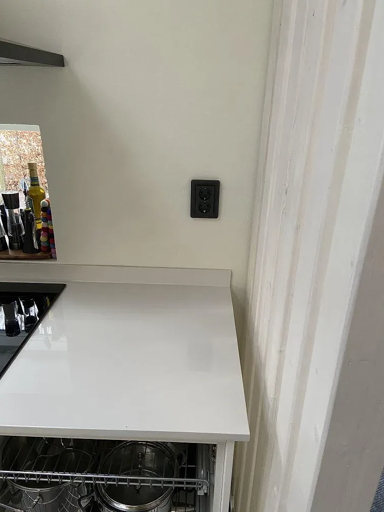 Hörn av polerad Dekton Halo keramikbänkskiva med svart eluttag och diskmaskin under i ett kök i Lund.