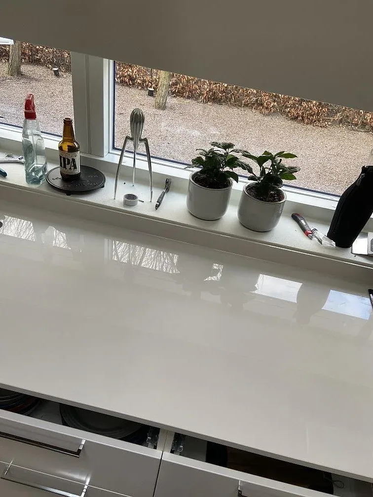 Polerad köksbänkskiva i Dekton Halo keramik längs fönstervägg med växter i fönstret i ett kök i Lund.