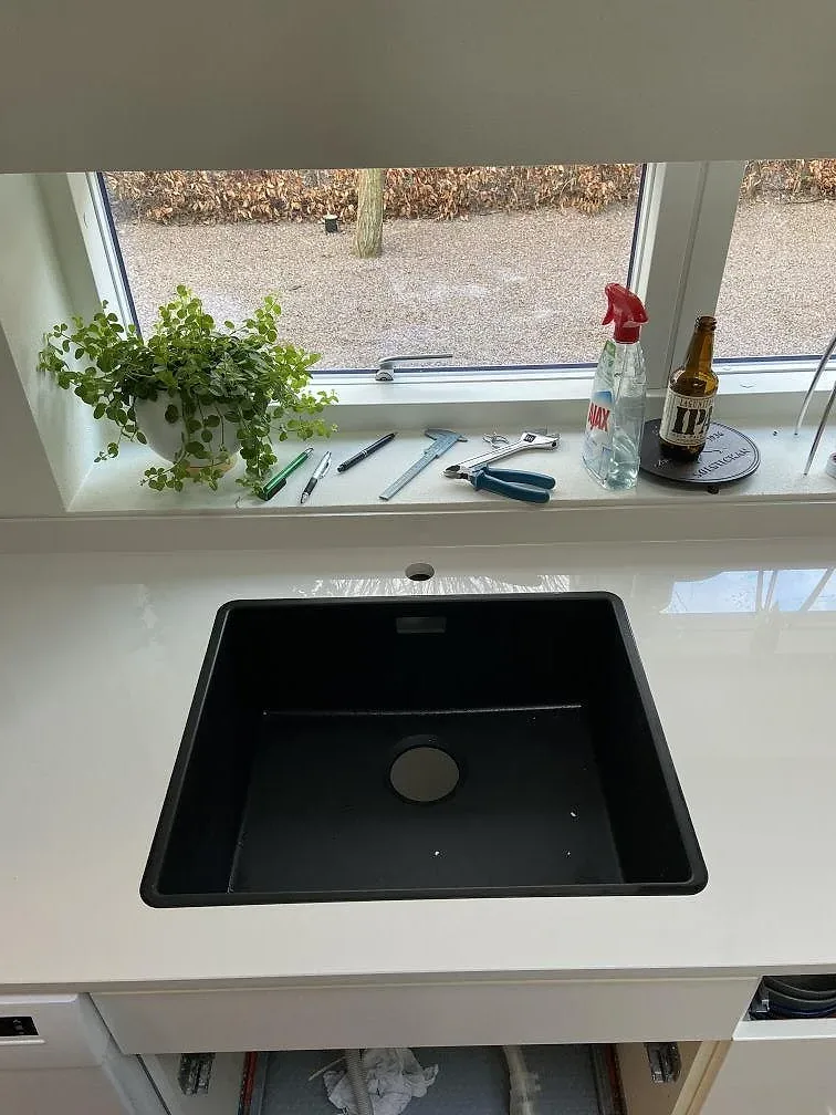 Underlimmad svart kompositdiskho i polerad Dekton Halo keramikbänkskiva med separat borrat blandarhål i ett kök i Lund.