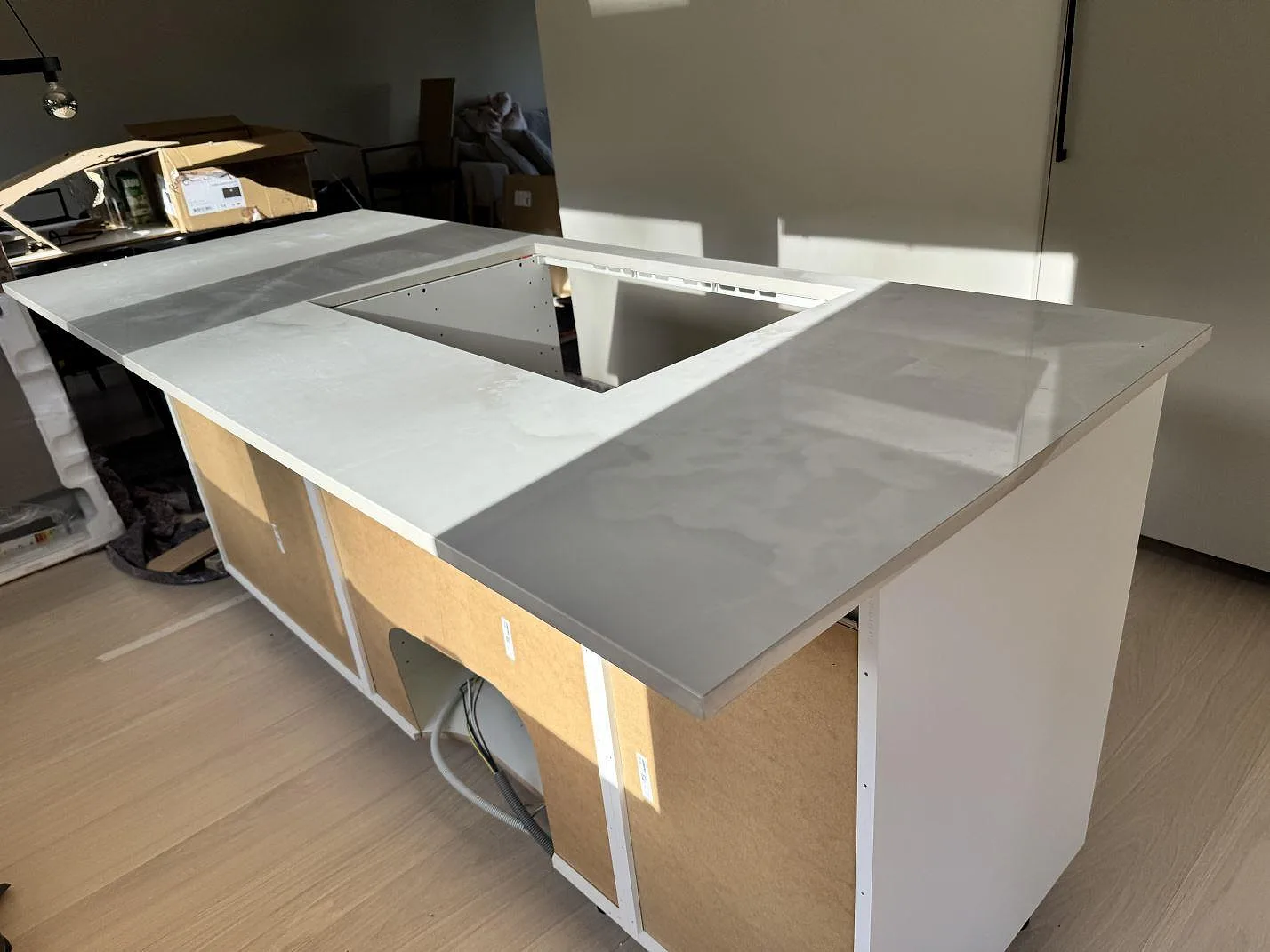 Köksö med polerad Dekton Helena i keramik, ljus sten och öppning i bänkskivan under montering i Göteborg.