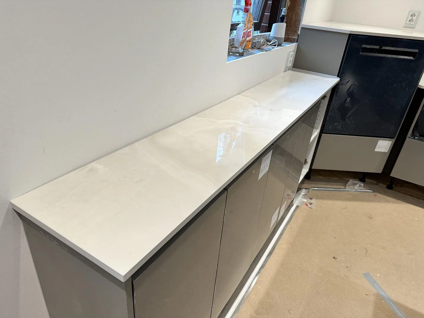 Lång köksbänk i polerad Dekton Helena med ljus ådring längs väggen i ett kök under montering i Helsingborg.