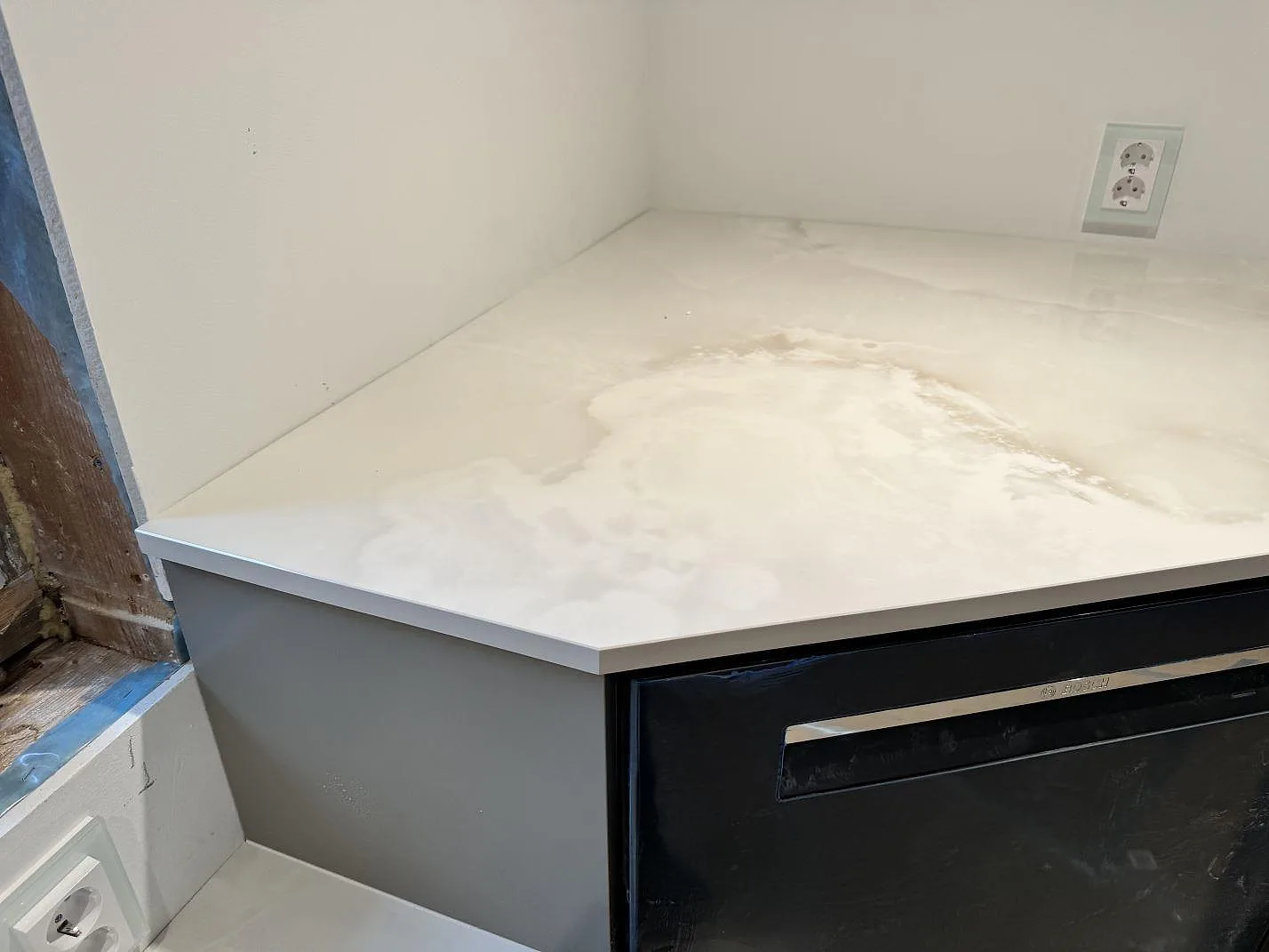 Närbild på hörnyta i polerad Dekton Helena med krämvit marmorering och mörka köksstommar i Helsingborg.
