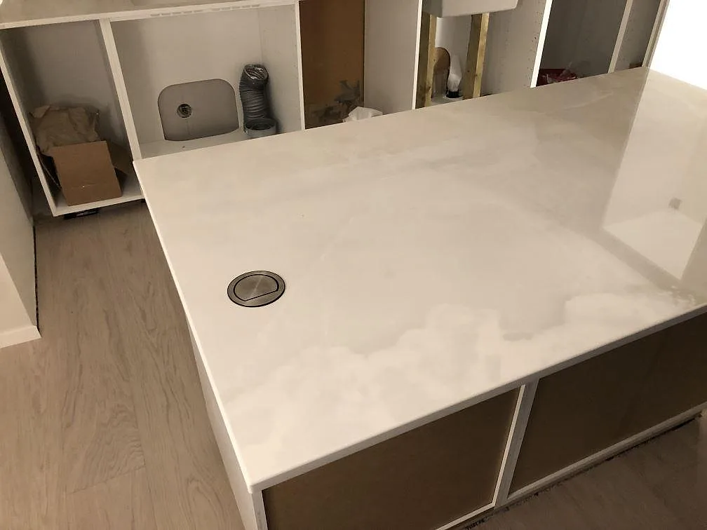 Köksö med högblank bänkskiva i Dekton Helena och borrat hål för avfallslucka, omgiven av köksstommar under installation i Lessebo.