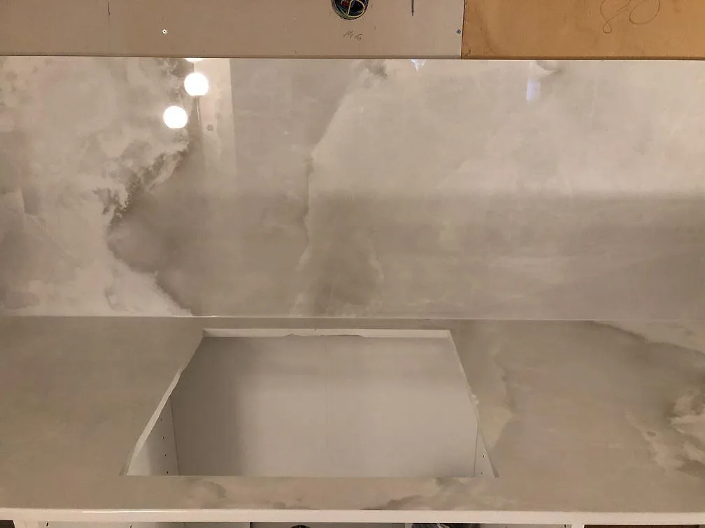 Vit Dekton Helena bänkskiva med onyxinspirerad ådring och uppvikt stänkpanel runt ett urtag för diskhon i ett kök i Lessebo.