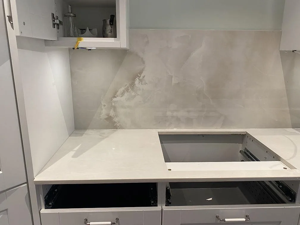 Köksbänkskiva i Dekton Helena med urtag för häll och heltäckande stänkvägg i gräddvit polerad keramik i ett kök i Ljungby.