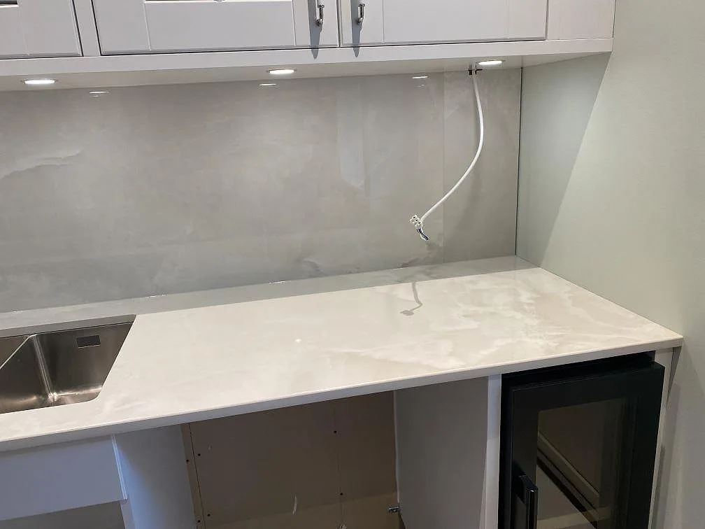 Köksbänkskiva i Dekton Helena med underlimmad rostfri diskho och heltäckande stänkvägg i polerad keramik i ett kök i Ljungby.