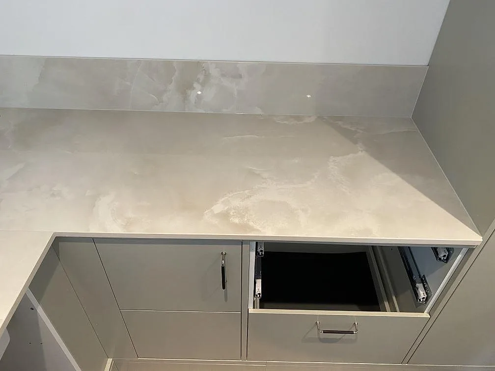 Polerad köksbänk i Dekton Helena keramik mot vägg med uppvikt stänkkant, ovanför ljusa köksstommar i Malmö.
