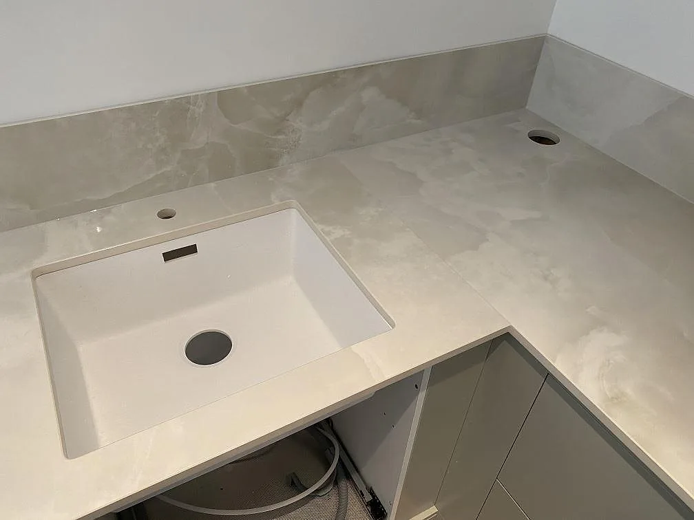 Underlimmad diskho i polerad Dekton Helena keramikbänk med kranhål och hörnskarvad stänkkant i ett kök i Malmö.