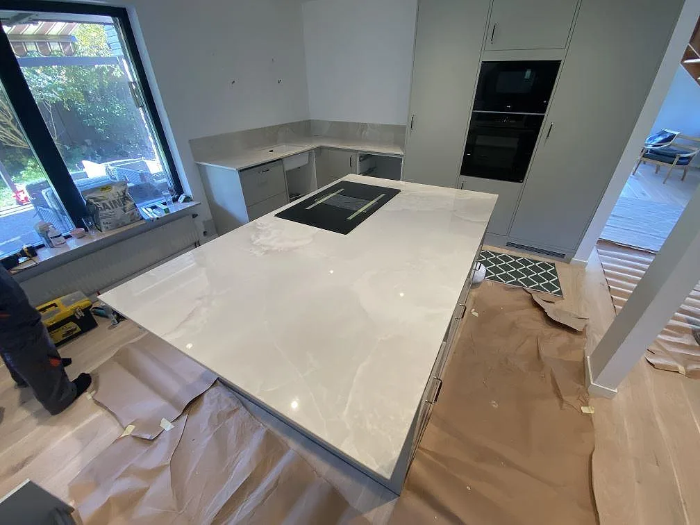 Köksbänkskiva i Dekton Helena, polerad gråbeige keramik med mjuk ådring, på en stor köksö med infälld induktionshäll i ett kök i Malmö.