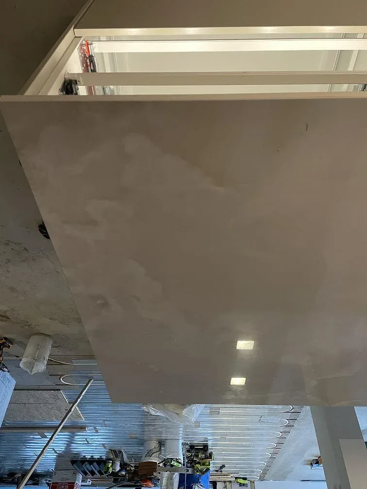 Köksö i polerad Dekton Helena med vit ådring och nedhängande gavel, fotad under montering i Ramlösa.