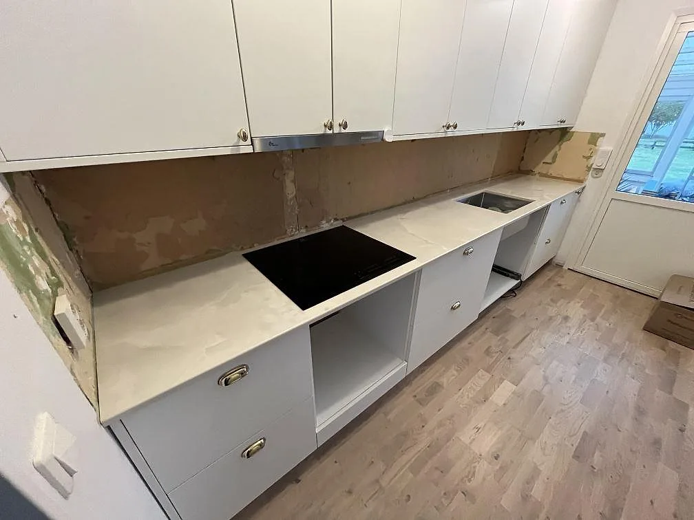 Köksbänkskiva i polerad Dekton Helena med svart induktionshäll och rostfri diskho under montering i Storebro.