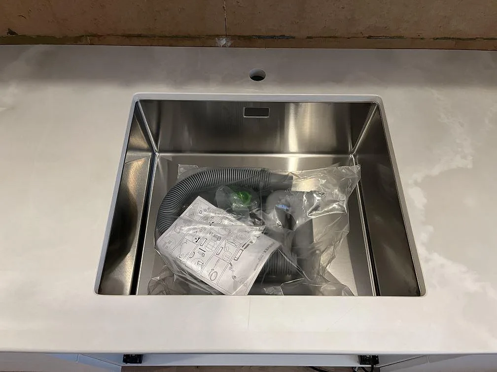 Underlimmad rostfri diskho i en polerad Dekton Helena köksbänkskiva med vit marmorlik ådring i Storebro.