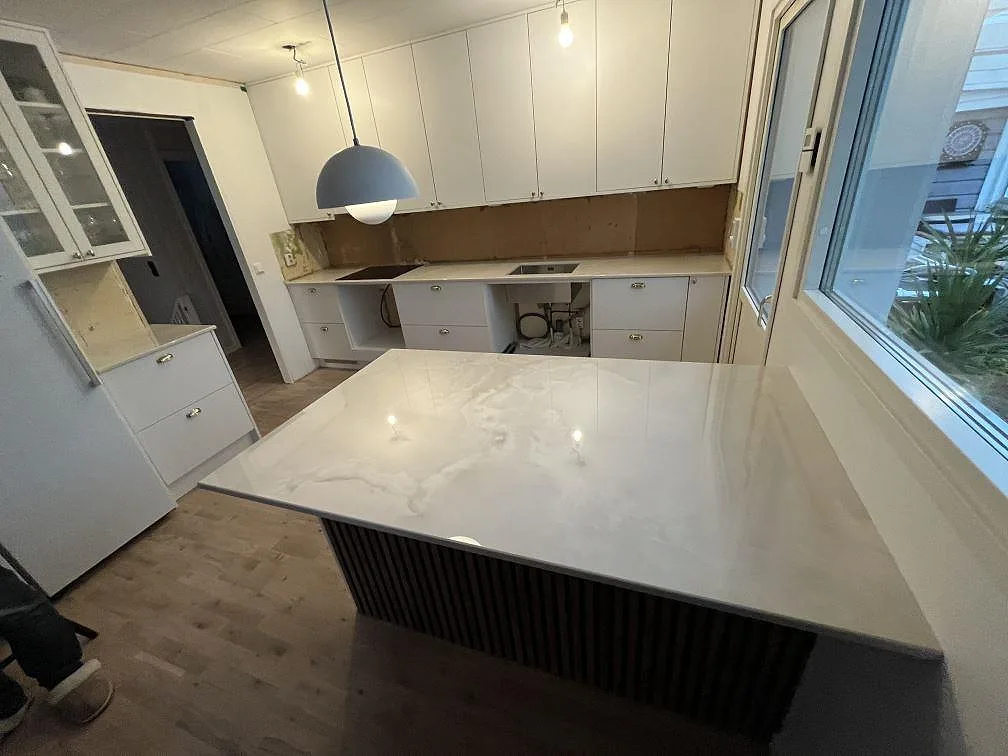 Stor köksö och köksbänkskiva i polerad Dekton Helena keramik med vit ådring i ett kök i Storebro.