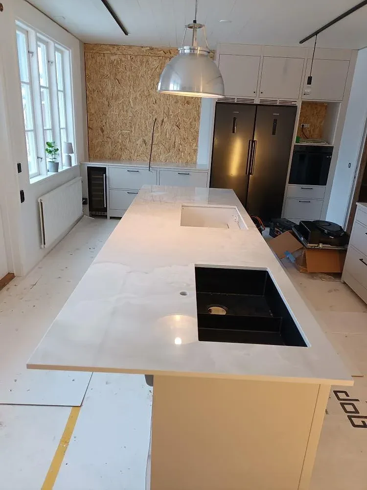 Polerad köksö i Dekton Helena med ljus grå ådring, synligt urtag och monteringsarbete i ett kök i Tranås.