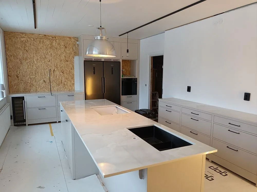 Köksbänkskiva och köksö i ljus Dekton Helena med grå ådring, polerad, med två underlimmade diskhoar i ett kök i Tranås.