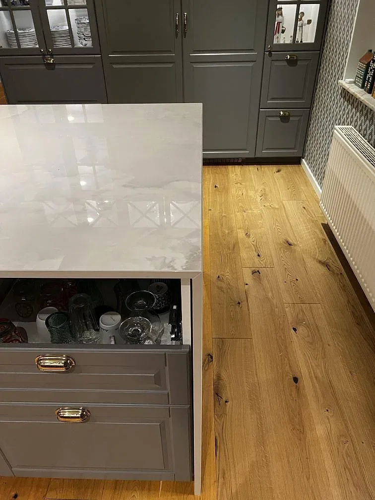 Närbild på polerad Dekton Helena köksö med blank vit ådring, grågröna köksluckor och trägolv i Växjö.
