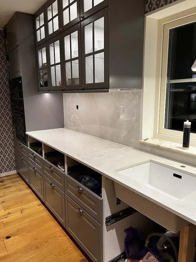 Väggbänk i polerad Dekton Helena med stänkskydd, vit diskho och öppna köksstommar under montering i Växjö.