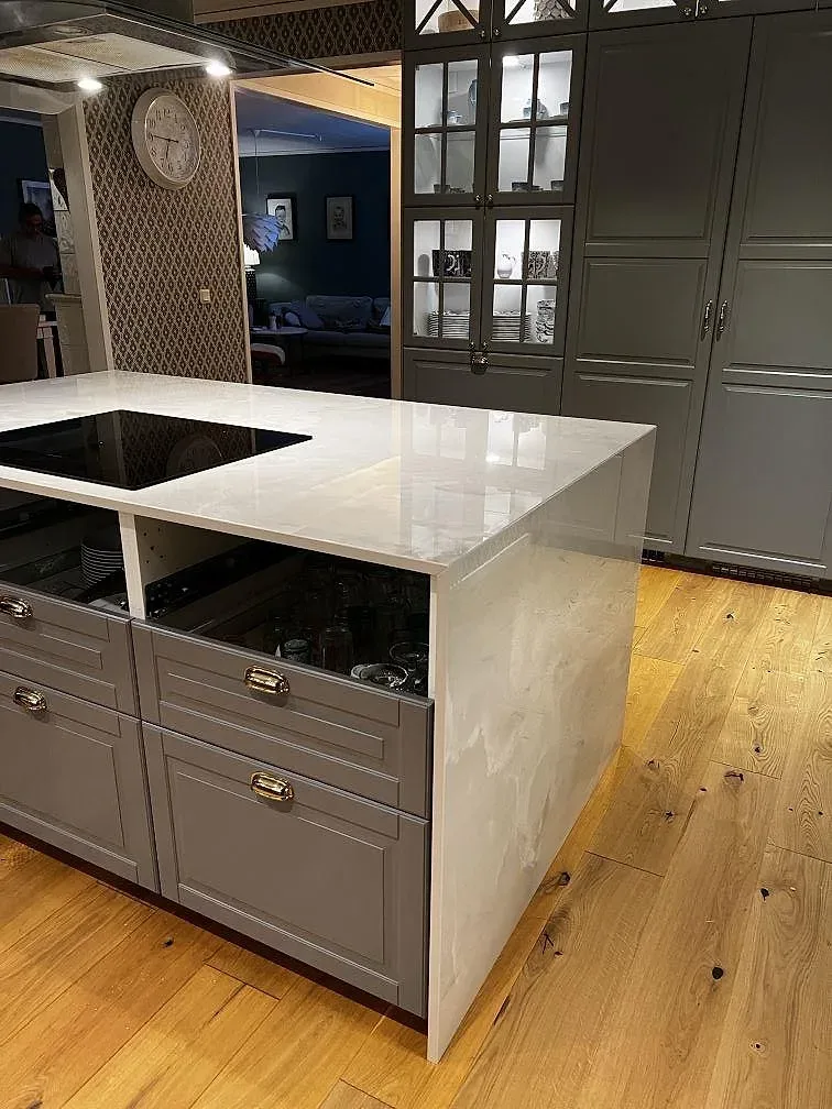 Stor köksö i polerad Dekton Helena keramik med vit ådring, svart häll, grågröna luckor och trävägg i Växjö.