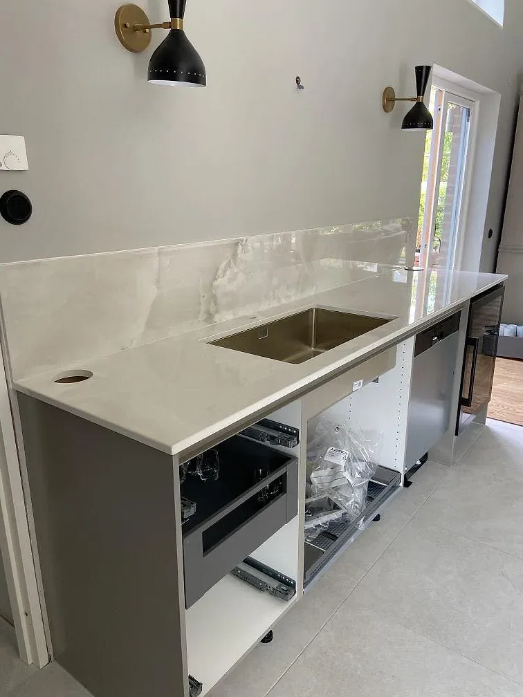 Underlimmad rostfri diskho i en polerad Dekton Helena-bänkskiva med matchande stänkskydd i ett kök i Ystad.