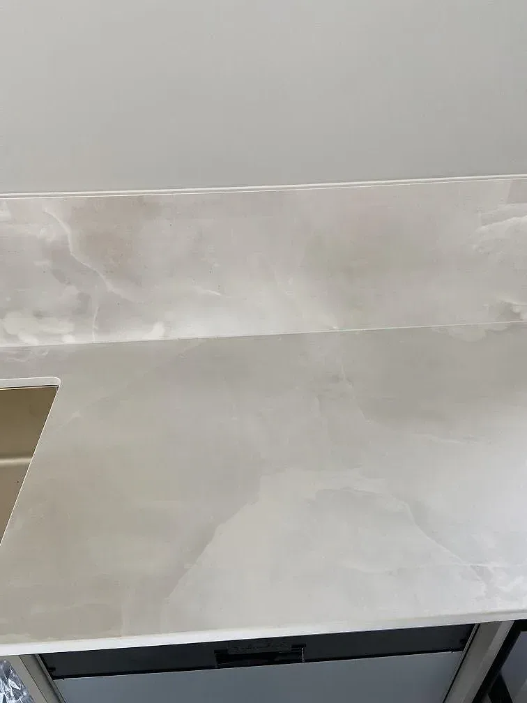 Lång köksö i vit polerad Dekton Helena med sittplats och barstolar i ett vardagsrumsöppet kök i Ystad.