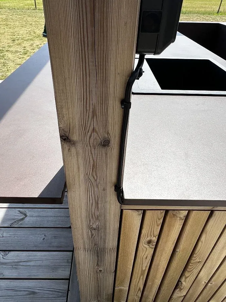 Detalj av matt Dekton Kadum bänkskiva vid svart diskho och trästolpe i ett utekök på trädäck i Påarp.
