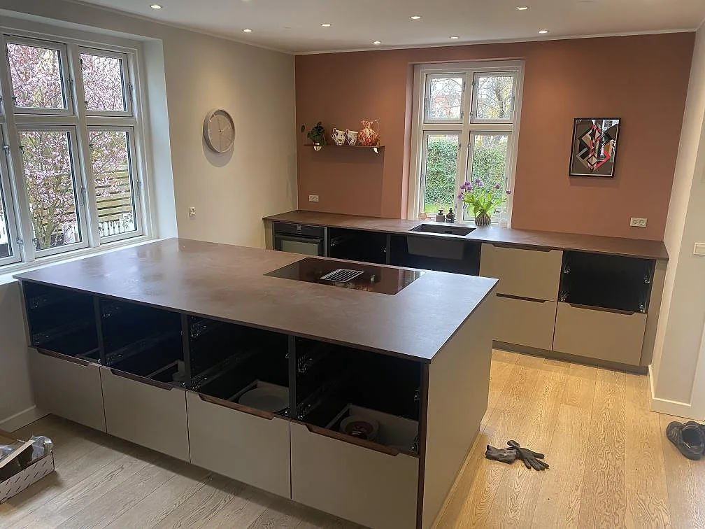Köksbänkskiva i Dekton Kadum, matt beige keramik, med stor köksö och induktionshäll med inbyggd fläkt i ett kök i Valby.