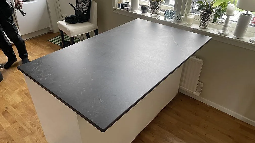 Köksö med bänkskiva i mörk matt Dekton Kelya keramik med ljus ådring, monterad vid fönster i ett kök i Askim.