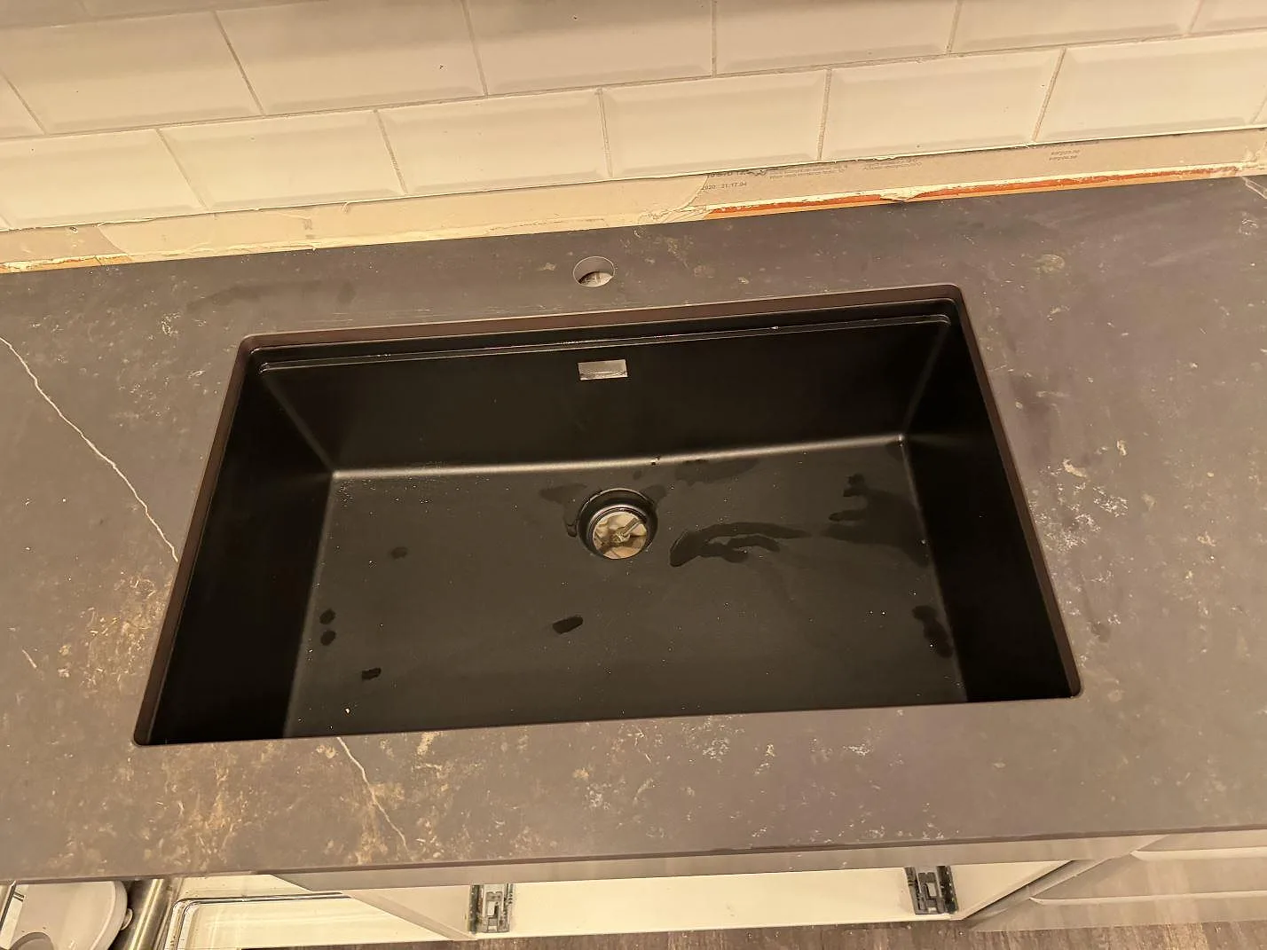 Svart diskho monterad ovanpå en matt köksbänkskiva i Dekton Kelya med vit kakelvägg i Borås.