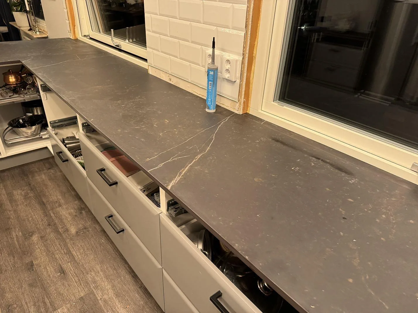 Lång köksbänkskiva i matt Dekton Kelya under fönster med ljus ådring och vit kakelvägg i Borås.