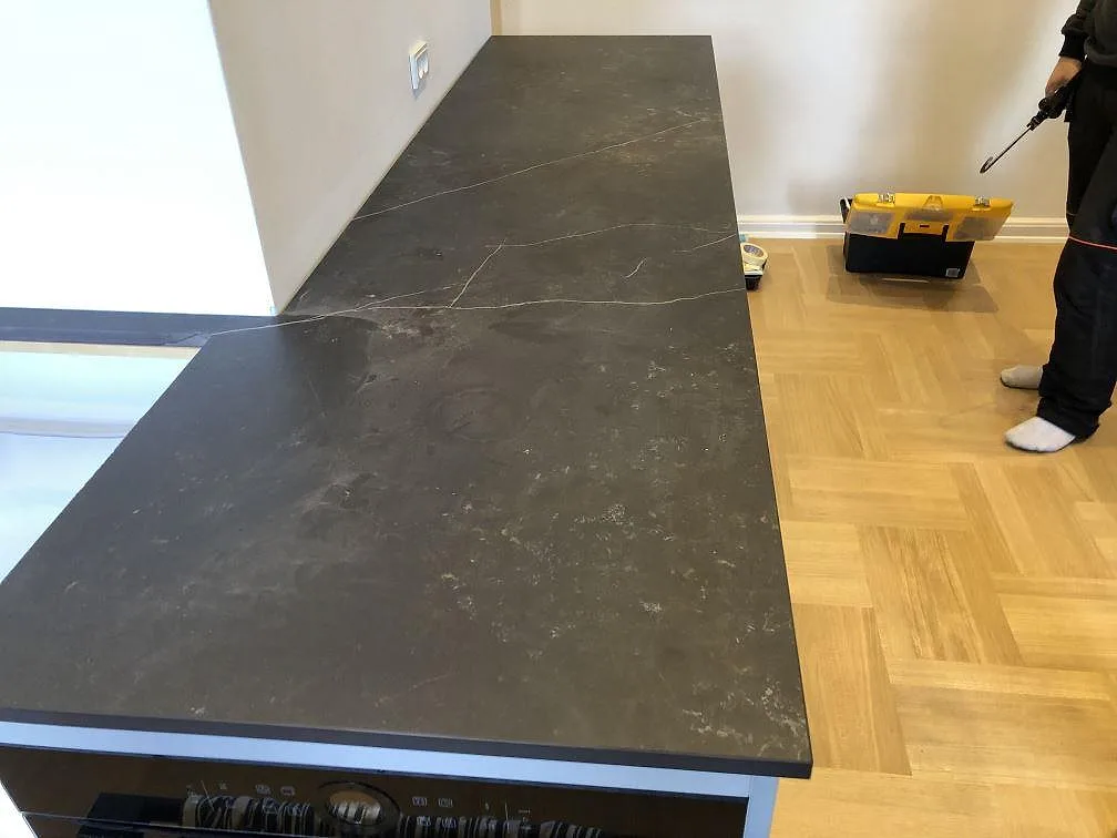 Lång rak köksbänkskiva i antracitsvart Dekton Kelya, matt, med diskret ljus ådring i ett kök under montering i Frederiksberg C.