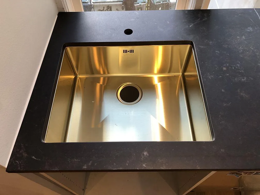 Undermonterad diskho i guldton i en matt köksbänkskiva av Dekton Kelya i Frederiksberg C.