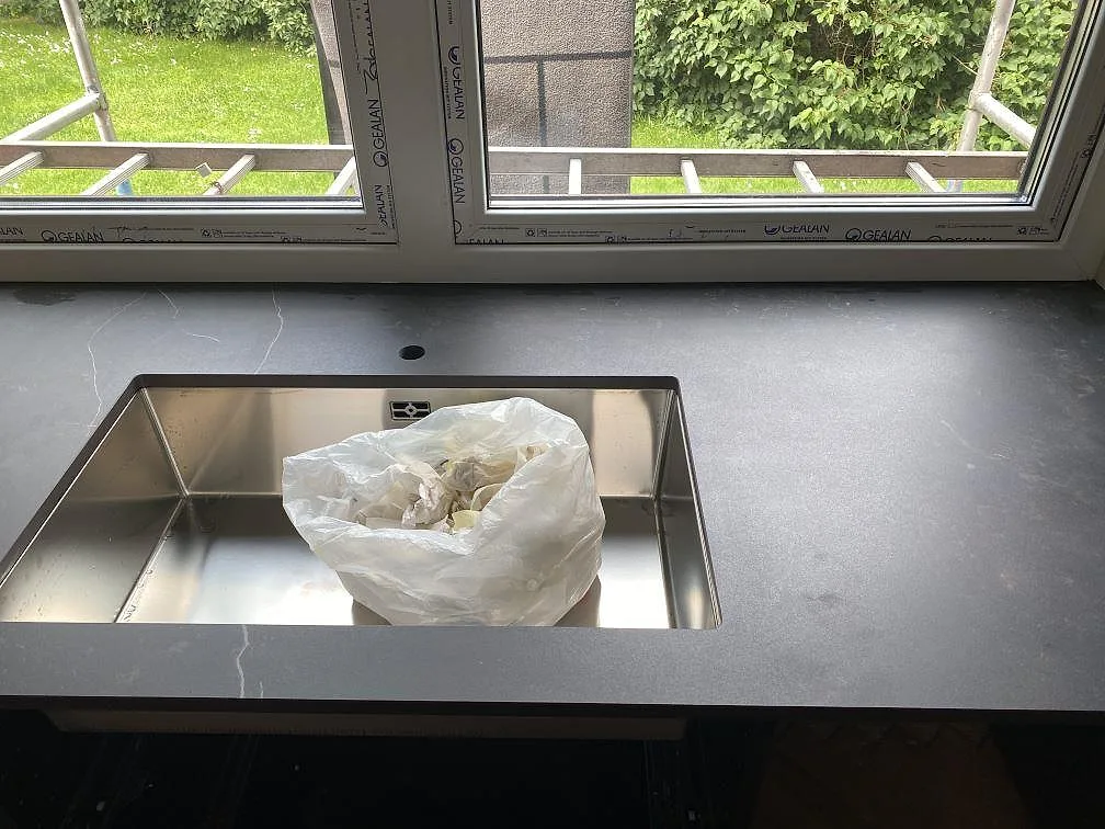 Underlimmad rostfri diskho i mörk Dekton Kelya köksbänkskiva framför fönstret i ett kök i Genarp.